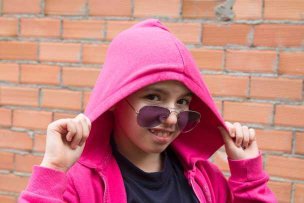 portrait of hipster girl with hoodie and sunglasses with brick wall background - Foto, Bild
