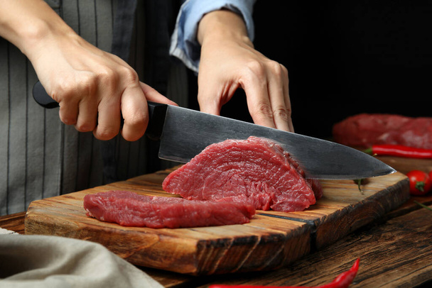 Woman cutting fresh raw meat at wooden table, closeup - Foto, afbeelding