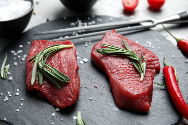 Fresh raw meat steaks and spices on slate plate, closeup - Photo, image