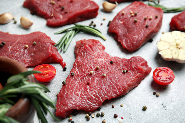 Fresh raw meat steaks and spices on light grey table, closeup - 写真・画像