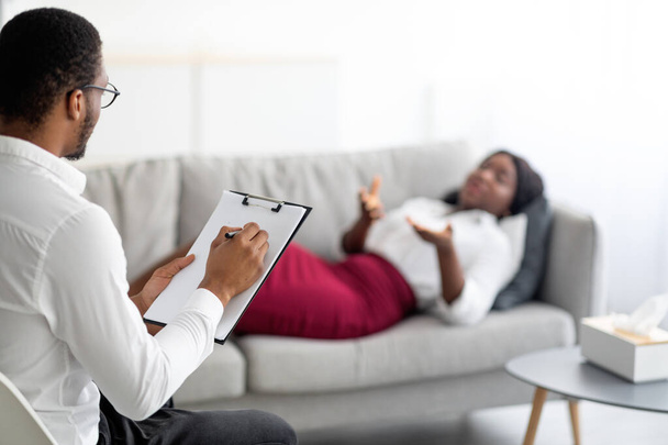 Joven mujer negra en consulta con el psicólogo, acostada en el sofá en la oficina, explicando su problema al médico - Foto, Imagen