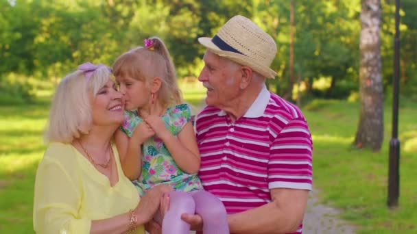 Little cute granddaughter child embracing with her grandmother and grandfather family couple in park - Filmmaterial, Video
