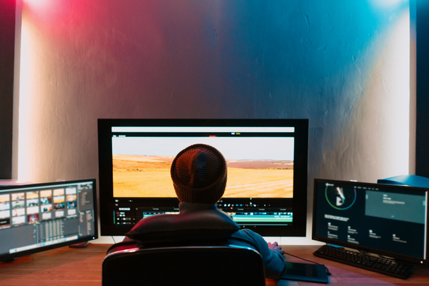 Αρσενικός επεξεργαστής βίντεο που εργάζεται στον προσωπικό υπολογιστή του με μεγάλη οθόνη - Φωτογραφία, εικόνα