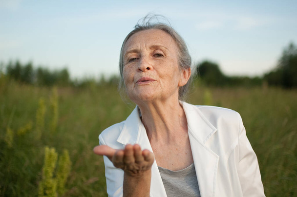 Porträt einer Seniorin mit grauen Haaren und faltenbehaftetem Gesicht, die weiße Jacke trägt und bei schönem Wetter im Park relaxt - Foto, Bild