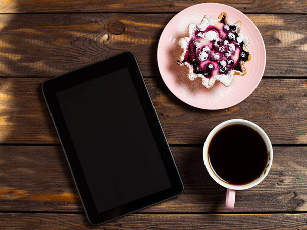 Flatley coffee break layout. Digital tablet gadget, black coffee in a cup and a cake basket with berries on a table from an old dark wood. - 写真・画像