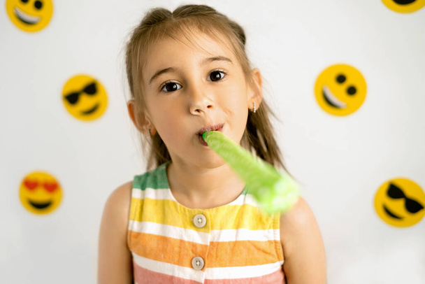 Une fille souffle une pipe festive sur un fond blanc avec une variété d'émoticônes. Journée mondiale des emoji. Sourire anthropomorphe Visage. - Photo, image