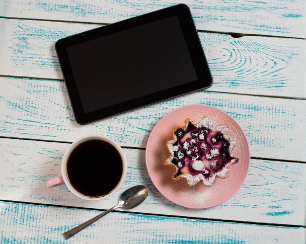 A digital tablet, a cup of coffee and a cake basket with berries and cottage cheese on a white and blue vintage table. Morning breakfast background. Flatley coffee break layout. - Photo, image