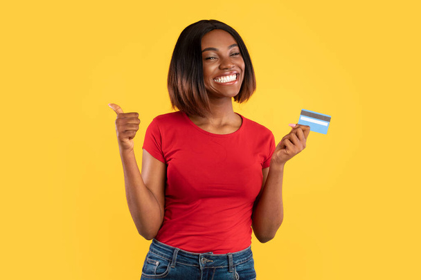 African American Lady Holding Credit Card Gesturing Thumbs-Up, Yellow Background - Photo, Image