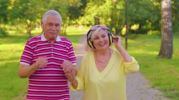 Пожилые стильные семейные пары бабушка дедушка танцует, слушая музыку в летнем парке - Кадры, видео