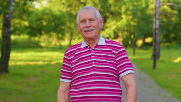 Šťastný půvabný starší šedovlasý dědeček v neformálním červeném tričku na pozadí letního parku - Záběry, video