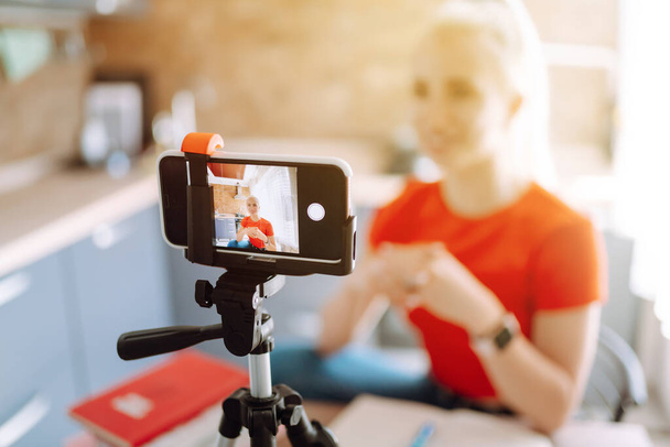 Young woman recording her video blog. Woman blogger videotapes her vlog at home. Vlogger makes online streaming using phone. Social media, instagram, stay home and quarantine. - Zdjęcie, obraz