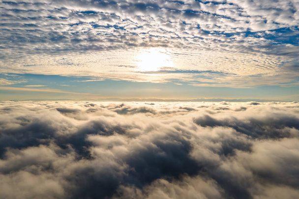 Widok z lotu ptaka żywy żółty wschód słońca nad białymi gęstymi chmurami z niebieskim niebem nad głową. - Zdjęcie, obraz