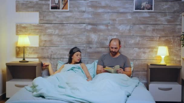 Young man reading a book while his wife is turning the lights off - Footage, Video