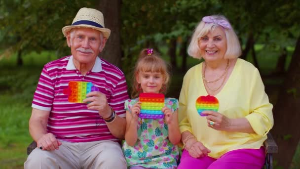 Senior élégant couple grand-mère grand-père avec petite-fille jouer anti-stress pop it jouet jeu - Séquence, vidéo