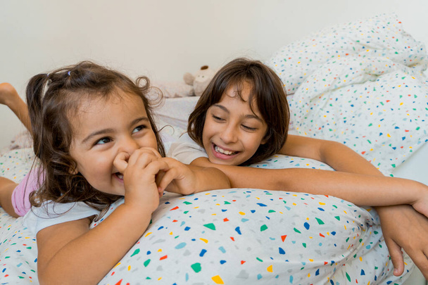 Két kaukázusi lány, két és kilenc évesek, jól érzik magukat együtt a hálószobájukban, játszanak és beszélgetnek.. - Fotó, kép