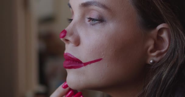 νεαρή γυναίκα ζωγραφίζει μακιγιάζ κλόουν στο πρόσωπό της - Πλάνα, βίντεο