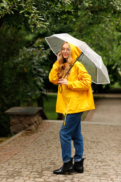 Счастливая женщина в жёлтом плаще с прозрачным зонтиком под дождём - Фото, изображение