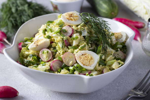 Салат с китайской капустой, огурец, редис, зеленый лук и перепелиные яйца в белой тарелке на сером фоне. - Фото, изображение