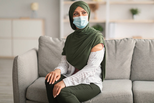 Mujer musulmana mostrando brazo con yeso después de la vacunación en casa - Foto, Imagen