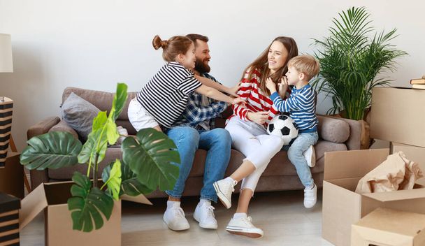 Χαρούμενα κορίτσι και αγόρι γαργαλώντας τους γονείς γέλιο ενώ στηρίζεται σε settee κοντά κουτιά από χαρτόνι και φυτά σε νέο διαμέρισμα - Φωτογραφία, εικόνα