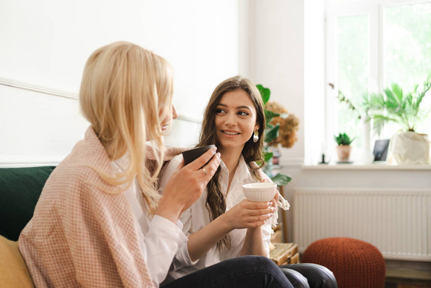 Mother with daughter drinking tea together in living room at home - Fotoğraf, Görsel
