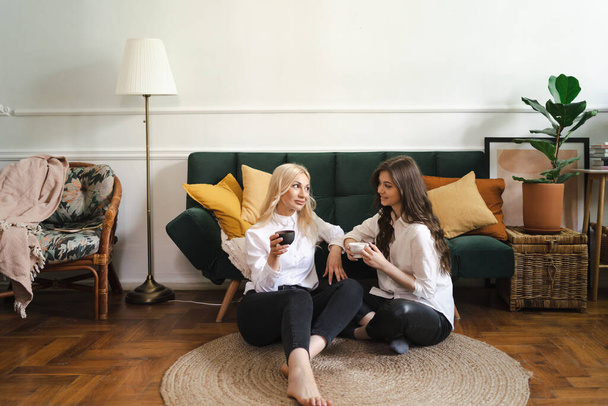 Mother with daughter drinking tea together in living room at home - Photo, Image