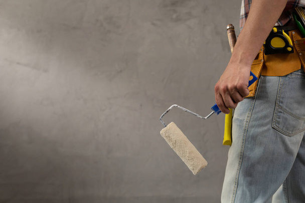 Construction worker man holding paint roller tool near concrete or plaster wall. Male hand and construction tools for house room renovation. Home renovation concept - Фото, зображення