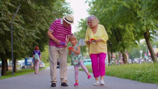 Büyük büyükanne büyükbaba torunuyla yürüyor ve stres karşıtı pop it oyuncak oyunu oynuyor. - Video, Çekim