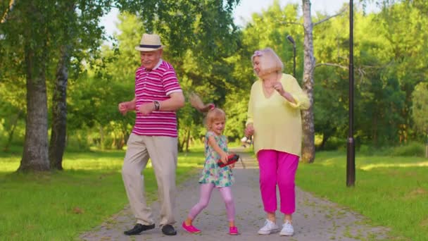 Granddaughter together with senior grandmother grandfather listening to music, dancing crazy in park - Footage, Video