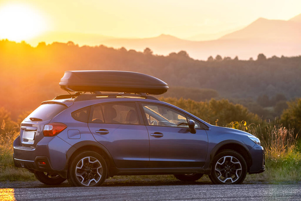 SUV car with roof rack luggage container for off road travelling parked at roadside at sunset. Road trip and getaway concept. - Photo, Image
