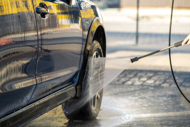 Крупный план водителя мужского пола, моющего машину бесконтактной струей воды высокого давления в автомойке самообслуживания. - Фото, изображение