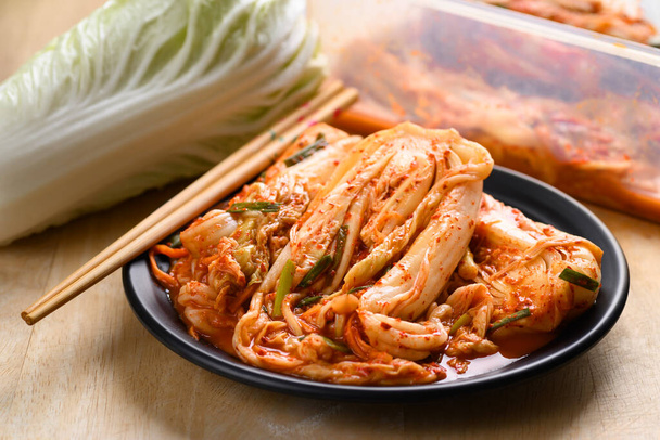 Капуста кимчи на тарелке с палочками, Популярные домашние корейские традиционные ферментированные гарниры - Фото, изображение