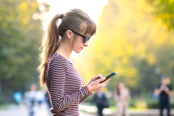 Jovem mulher bonita usando seu telefone celular no dia quente de verão ao ar livre. - Foto, Imagem
