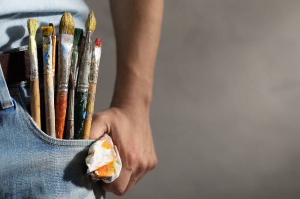 Used paintbrush in jeans pocket of painter artist. Paint brush for oil painting as art concept near wall background - Fotoğraf, Görsel