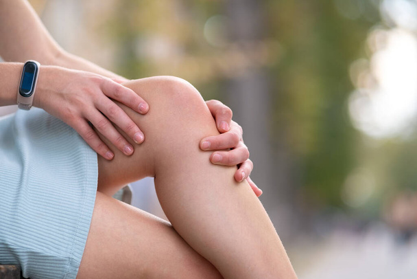 close-up van vrouw handen houden haar knie in pijn zittend op bank buiten. - Foto, afbeelding
