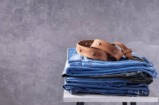 Denim jeans and leather belt at chair. Stack of jeans near abstract background texture surface - Photo, Image