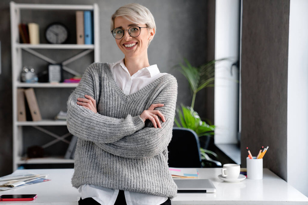 White-haired smiling woman looking at camera while standing in office - Foto, imagen