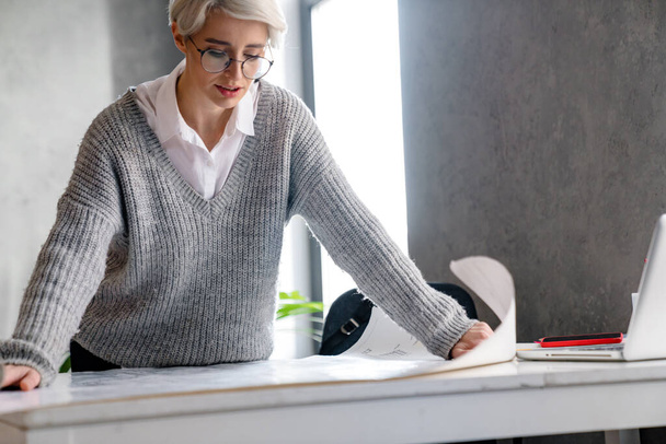 White-haired focused woman examining drawing while standing in office - Foto, Bild