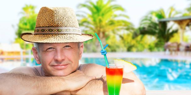 Un hombre está disfrutando de sus vacaciones relajándose con refrescante bebida en la piscina en el fondo del hotel resort. - Foto, imagen