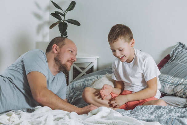 Apa 7-10-re játszik a fiával az ágyban. Apa nézz a gyerekre és mosolyogj. A fiú nevet. A család jól érzi magát - Fotó, kép