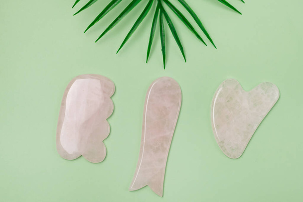 Close Up Cosmetic Massage Pink Jade Gua Sha Scrapers for Facial and Body Skin Care Spa and Beauty Concept Green Background Flat Lay - 写真・画像