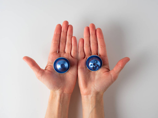 Dans les mains des hommes sont deux capsules de café en aluminium bleu. Une des gélules est utilisée. Fond blanc. Concept de réutilisation des matières premières - Photo, image