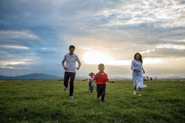 Asijská rodina kráčí a běží na louce při západu slunce se šťastnými emocemi. Koncept rodiny, dovolené a cestování. - Fotografie, Obrázek