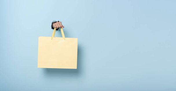 女性の手の青のバナーの背景に紙のショッピングバッグを保持。割引や販売の概念.パノラマ画像 - 写真・画像