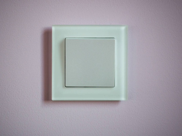 Um interruptor elétrico de um botão em uma moldura de vidro em uma parede rosa. - Foto, Imagem