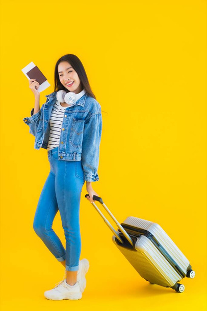 Портрет красивая молодая азиатка путешествия и отдыха с багажной сумкой и паспортом, посадочный талон на желтом изолированном фоне
 - Фото, изображение