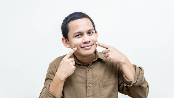 Portrait d'un jeune Malais asiatique pointant vers sa bouche pour sourire. Gardez positif. - Photo, image