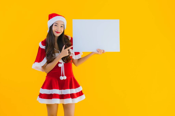 肖像画美しい若いアジアの女性クリスマス服と帽子の笑顔とともに空の白いボードサインオン黄色隔離された背景 - 写真・画像