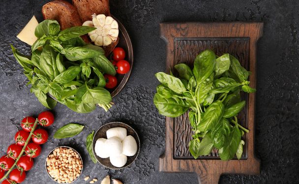 Italian cuisine. Preparation, cooking process. Ingredients: basil, mozzarella, tomatoes, garlic, parmesan cheese, bruschetta, pine nuts on a dark table. Background image, copy space. Flatlay, top view - Фото, изображение