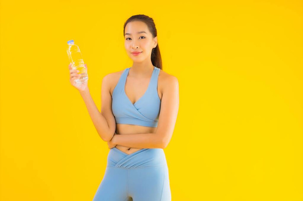 Sarı izole edilmiş arka planda su şişesiyle güzel bir Asyalı kadın portresi. - Fotoğraf, Görsel